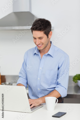Photo: Man using a laptop in the kitchen Man using a laptop in the kitchen