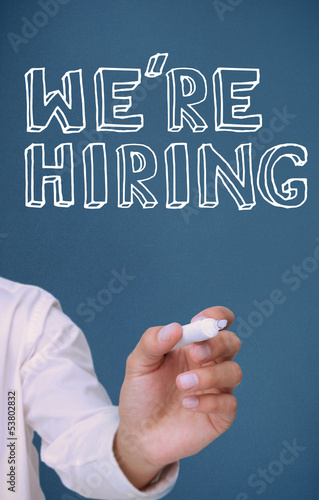Photo: Hand holding a marker and writing we're hiring Hand holding a marker and writing we're hiring