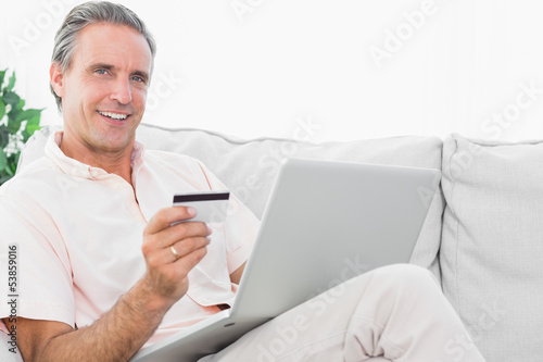 Photo: Happy man on his couch using laptop for shopping online Happy man on his couch using laptop for shopping online