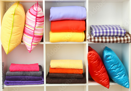 Photo: Bright pillows, towels and plaids on shelves, isolated on white Bright pillows, towels and plaids on shelves, isolated on white