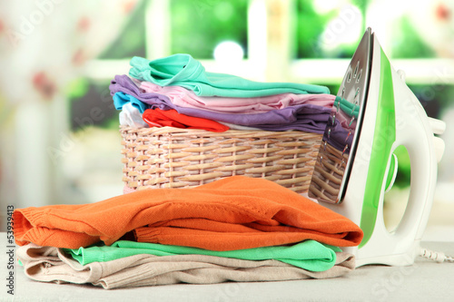 Photo: Steam iron and wicker basket with clothes, on bright background Steam iron and wicker basket with clothes, on bright background