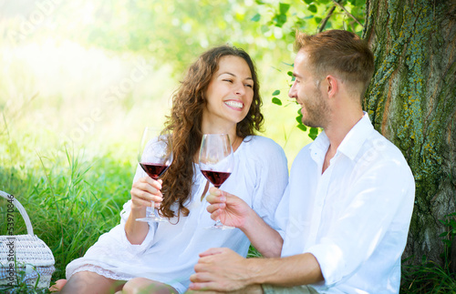 Photo: Picnic. Young Couple relaxing and drinking Wine in a Park Picnic. Young Couple relaxing and drinking Wine in a Park
