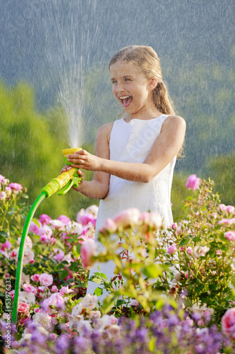 Photo: Summer garden, girl watering roses with garden hose Summer garden, girl watering roses with garden hose