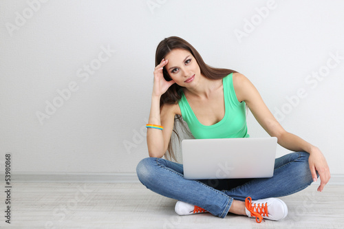 Photo: Beautiful young woman sitting with laptop in room Beautiful young woman sitting with laptop in room