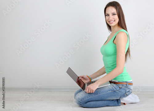 Photo: Beautiful young woman sitting with laptop in room Beautiful young woman sitting with laptop in room