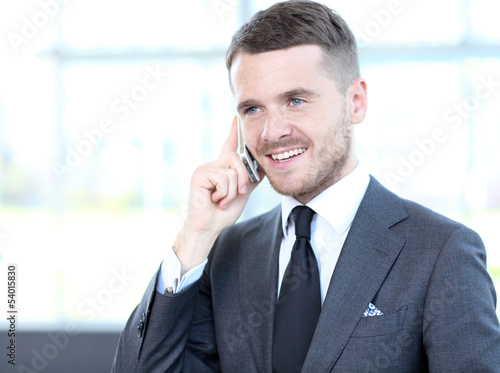 Photo: A young handsome business man on phone at office building A young handsome business man on phone at office building