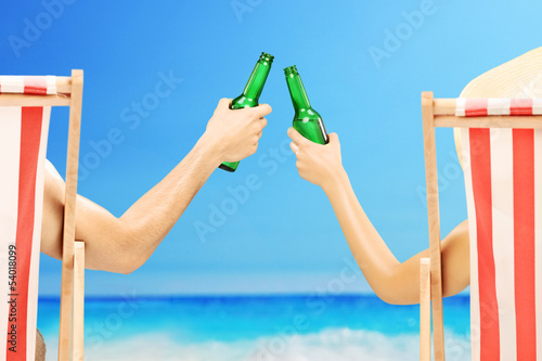 Photo: Man and woman relaxing on a beach and cheering with beer Man and woman relaxing on a beach and cheering with beer