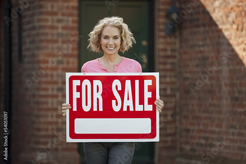 Photo: A mature woman holding a property for sale sign A mature woman holding a property for sale sign