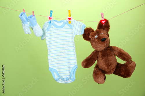 Photo: Baby clothes hanging on clothesline, on green background Baby clothes hanging on clothesline, on green background