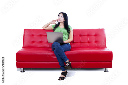 Photo: Thoughtful female using laptop on red sofa - isolated Thoughtful female using laptop on red sofa - isolated