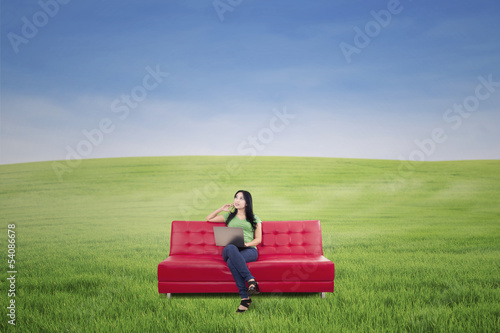 Photo: Thoughtful woman on red sofa at green field Thoughtful woman on red sofa at green field