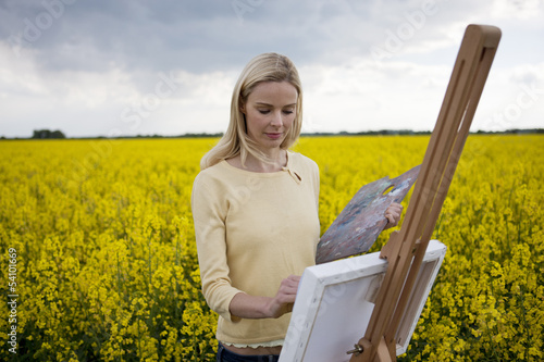 Photo: A young woman painting a picture of a rape seed field in flower A young woman painting a picture of a rape seed field in flower