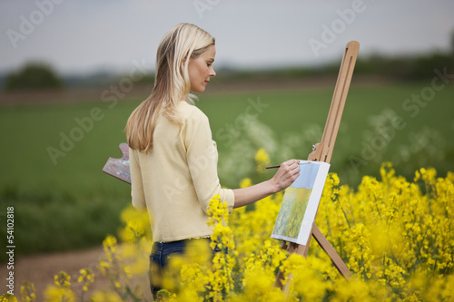Photo: A young woman painting a picture of a rape seed field A young woman painting a picture of a rape seed field