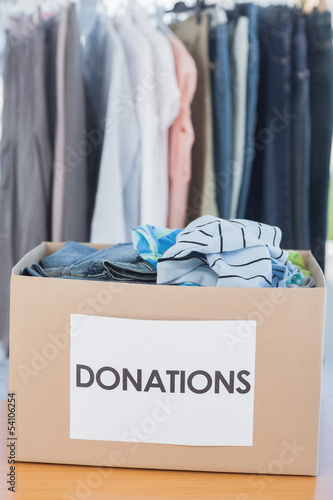 Photo: Donations box full of clothes in front of clothes rail Donations box full of clothes in front of clothes rail