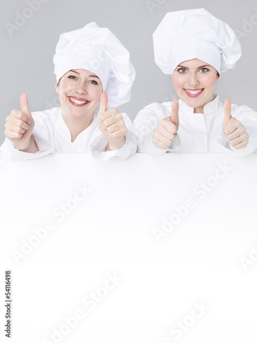 Photo: Female cooks show white blackboard with copyspace Female cooks show white blackboard with copyspace