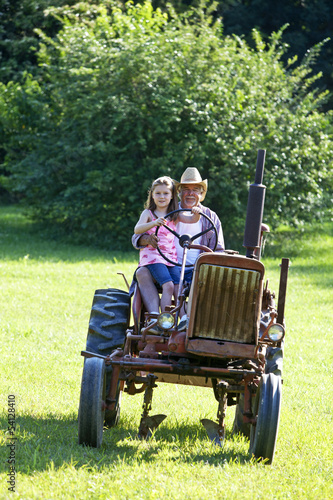 Photo: Young girl with grandfather driving a tractor on a farm Young girl with grandfather driving a tractor on a farm