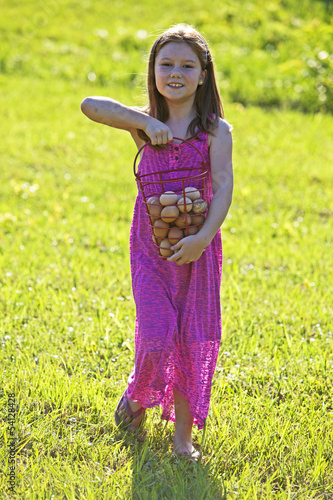 Photo: Young girl carrying brown eggs in a basket Young girl carrying brown eggs in a basket