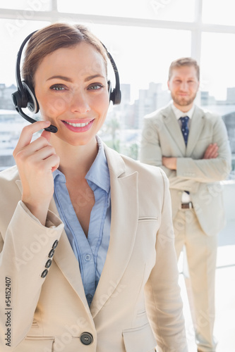 Photo: Smiling call centre agent with colleague behind her Smiling call centre agent with colleague behind her