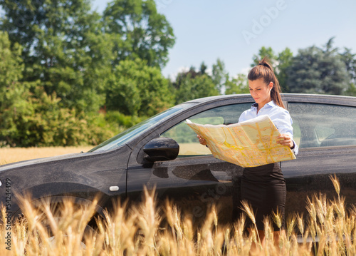Photo: Woman lost with car in a corn field and looking at the map Woman lost with car in a corn field and looking at the map