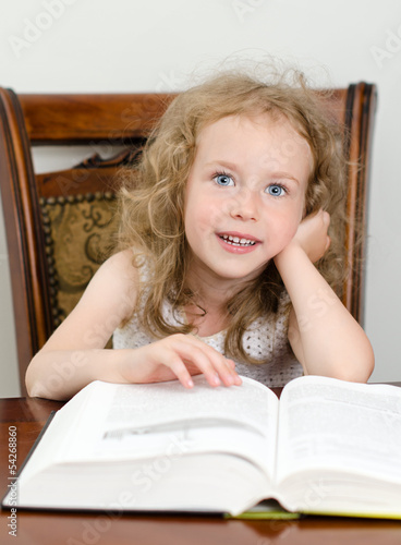 Photo: Cute little smiling girl reading a book Cute little smiling girl reading a book