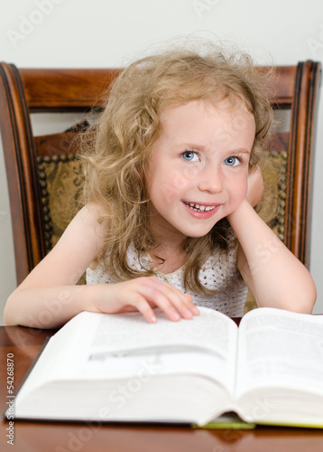 Photo: Cute little smiling girl reading a book Cute little smiling girl reading a book