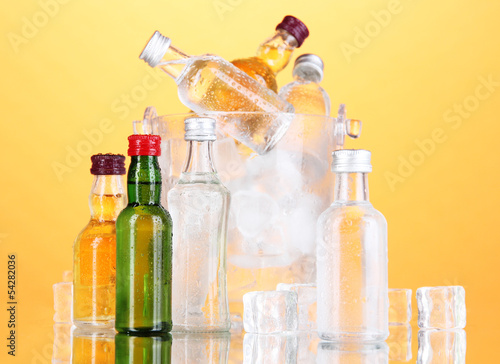 Photo: Minibar bottles in bucket with ice cubes, on color background Minibar bottles in bucket with ice cubes, on color background