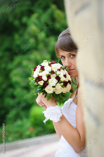 Photo: pensive bride in white dress standing and holding roses bouquet pensive bride in white dress standing and holding roses bouquet