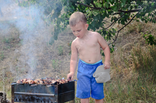 Photo: Little boy turning kebabs over the fire Little boy turning kebabs over the fire