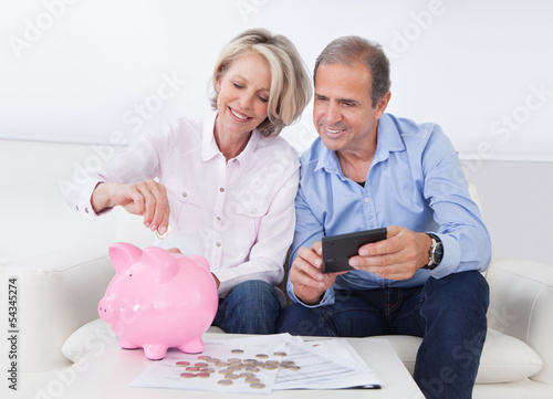 Photo: Mature Couple Calculating Coin In The Piggybank Mature Couple Calculating Coin In The Piggybank