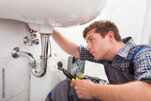 Photo: Young plumber fixing a sink in bathroom Young plumber fixing a sink in bathroom