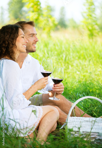 Photo: Picnic. Young Couple relaxing and drinking Wine in a Park Picnic. Young Couple relaxing and drinking Wine in a Park