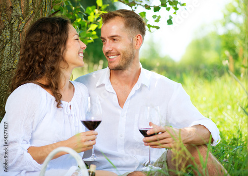 Photo: Picnic. Young Couple relaxing and drinking Wine in a Park Picnic. Young Couple relaxing and drinking Wine in a Park