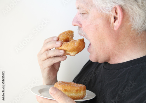 Photo: older man eats glazed doughnut older man eats glazed doughnut