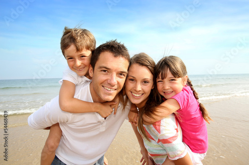 Photo: Parents giving piggyback ride to kids at the beach Parents giving piggyback ride to kids at the beach