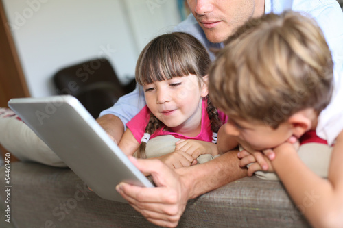 Photo: Father and children playing with tablet at home Father and children playing with tablet at home