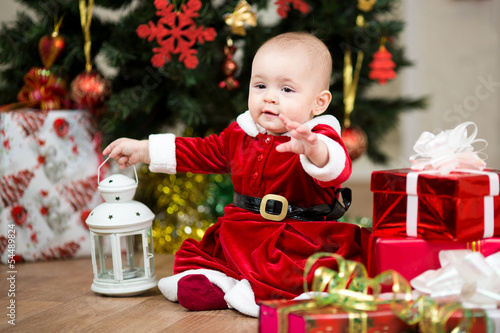 Photo: baby girl dressed as Santa Claus in front of Christmas tree with baby girl dressed as Santa Claus in front of Christmas tree with
