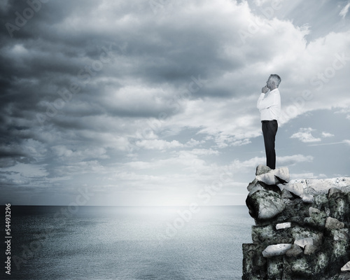 Photo: Thoughtful businessman standing at the edge of a cliff Thoughtful businessman standing at the edge of a cliff