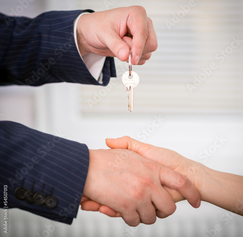 Photo: Male realtor giving a key of a new family house to a client Male realtor giving a key of a new family house to a client