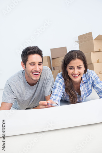 Photo: Happy couple lying on the floor and holding a house plan Happy couple lying on the floor and holding a house plan