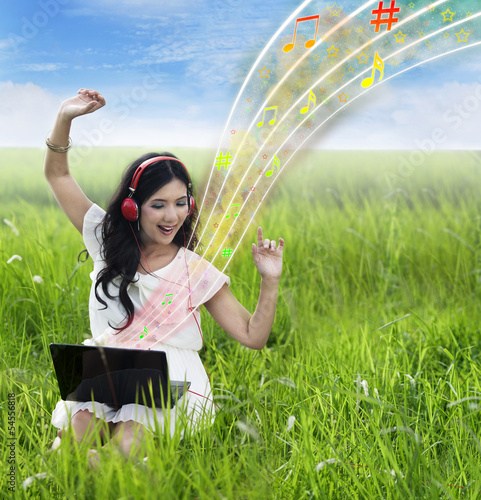 Photo: Beautiful female listening to music on laptop - outdoor Beautiful female listening to music on laptop - outdoor