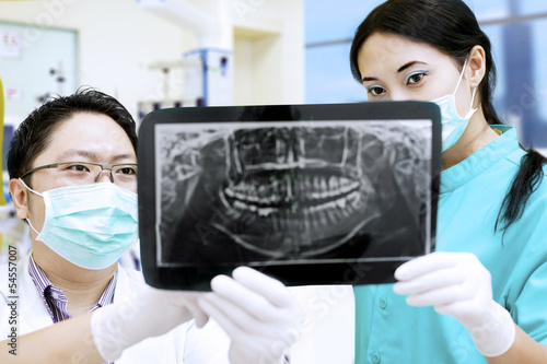 Photo: Attractive assistant and dentist looking at x-ray at hospital Attractive assistant and dentist looking at x-ray at hospital