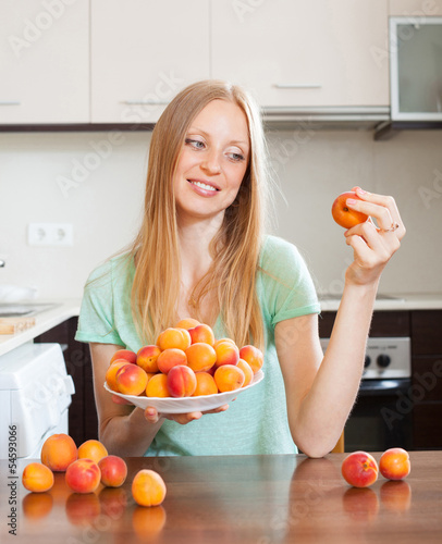 Photo: blonde long-haired woman eating apricots in home kitchen blonde long-haired woman eating apricots in home kitchen