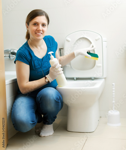 Photo: Smiling housewife cleaning toilet bowl with sponge Smiling housewife cleaning toilet bowl with sponge