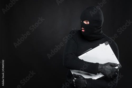 Photo: Stealing a suitcase. Frustrated thief in black balaclava holding Stealing a suitcase. Frustrated thief in black balaclava holding