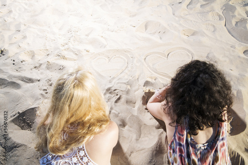 Photo: Two young womans draw hearts on sand. Two young womans draw hearts on sand.