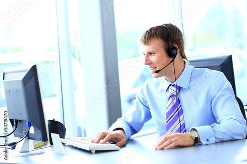 Photo: Happy young man working at callcenter, using headset Happy young man working at callcenter, using headset