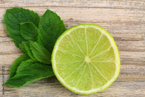 Photo: Lime with mint leaves on wooden surface, close up Lime with mint leaves on wooden surface, close up