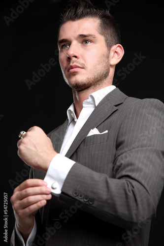 Photo: elegant fashion man looking at his cufflinks while fixing them elegant fashion man looking at his cufflinks while fixing them