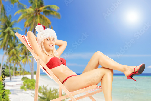 Photo: Young female in a santa costume sitting on a sun lounger on a be Young female in a santa costume sitting on a sun lounger on a be