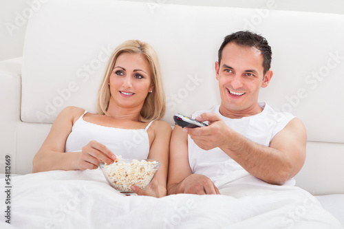Photo: Couple Relaxing On Bed With A Popcorn Watching Television Couple Relaxing On Bed With A Popcorn Watching Television
